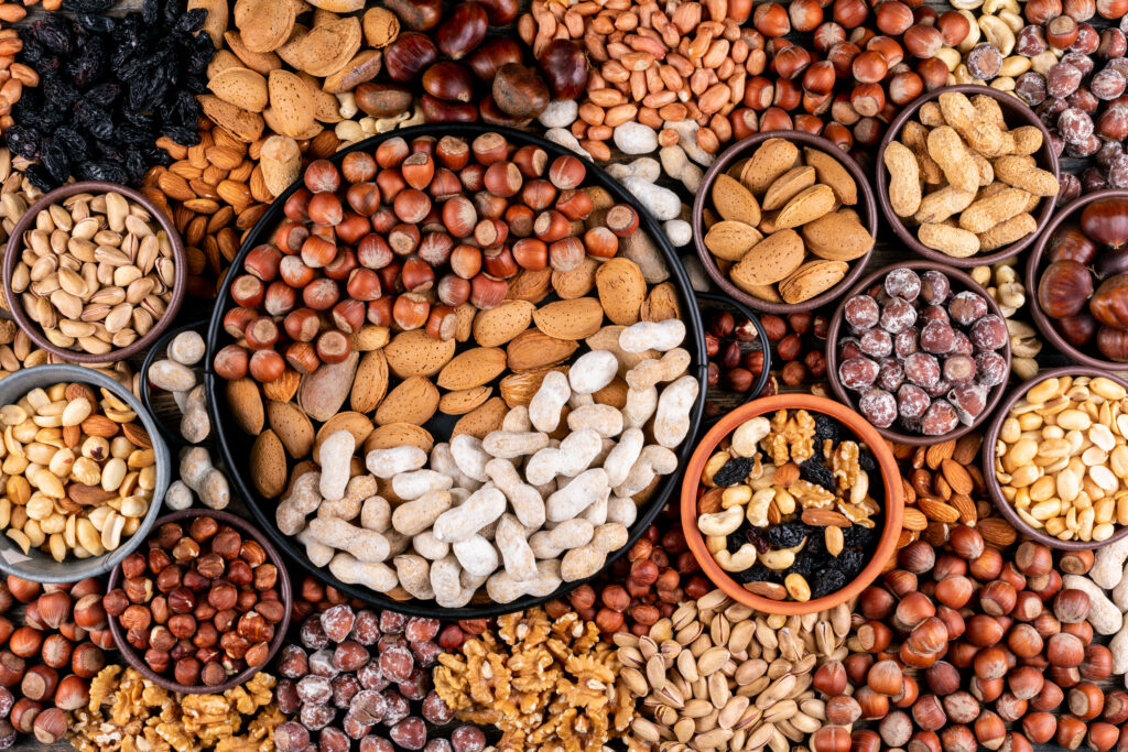 some of assorted nuts and dried fruits with pecan, pistachios, almond, peanut, cashew, pine nuts in a different bowls and black pan flat lay. some of assorted nuts and dried fruits with pecan, pistachios, almond, peanut, cashew, pine nuts in a different bowls and black pan flat lay.